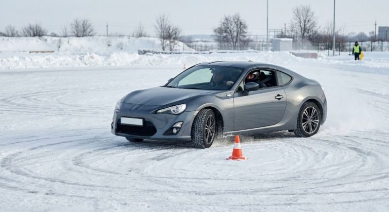 Сіре спортивне авто дрифтує на сніговому автодромі навколо конуса.